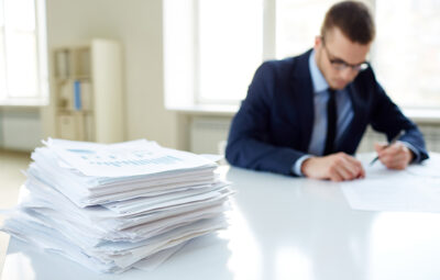 Stack of documents on the desk and male employee working on background